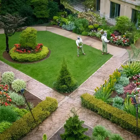 Gepflegter Garten mit Rasenfläche, Blumenbeeten und zwei Gärtnern bei der Arbeit.
