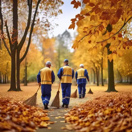 Arbeiter fegen Laub im herbstlichen Park, Herbstpflege und Reinigung öffentlicher Anlagen.